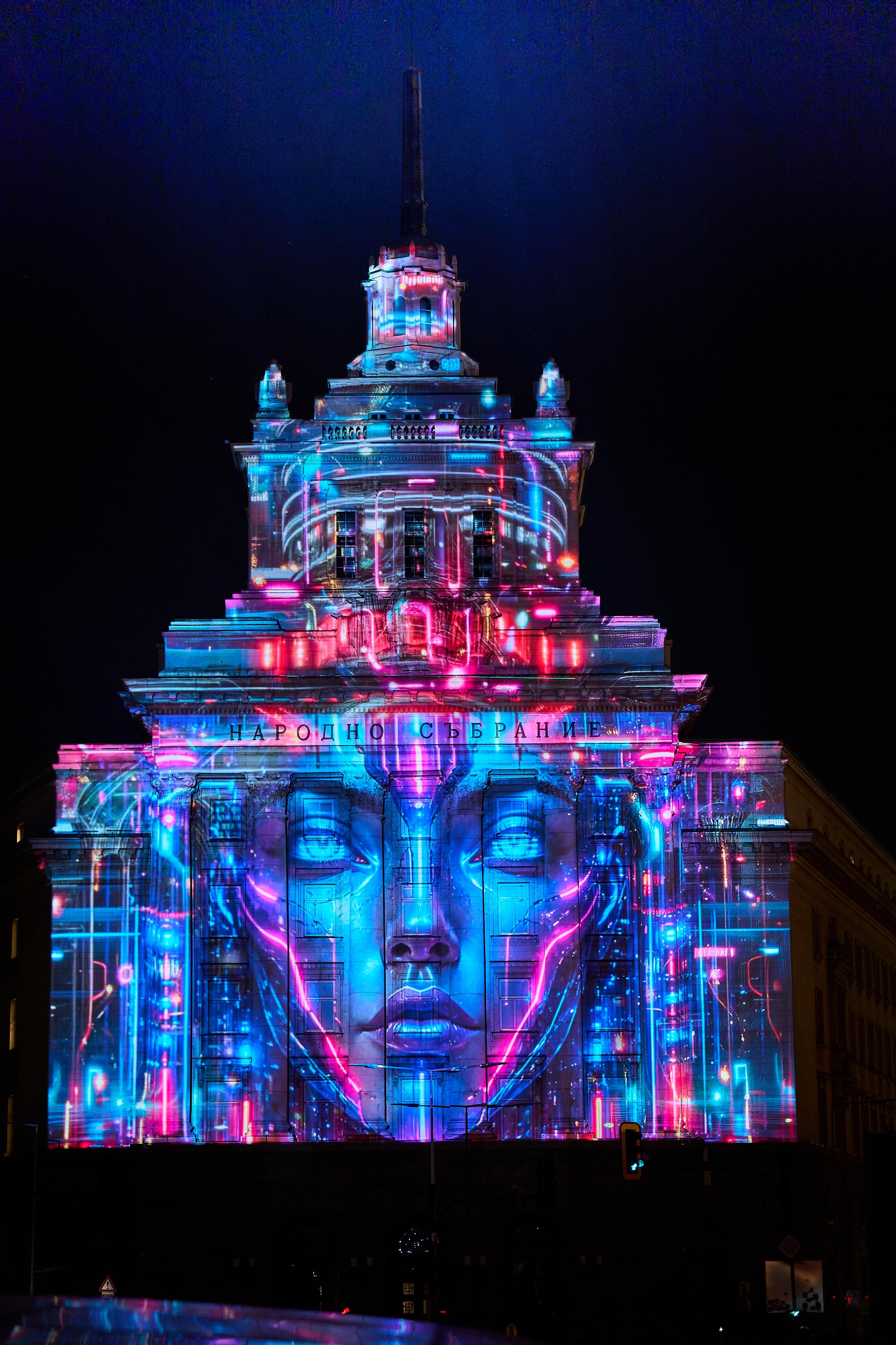 Blue and pink face imagery mapped onto the National Assembly facade at LUNAR 2026, Sofia